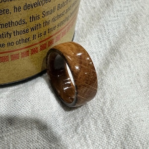 Puede incluir: Un anillo de madera de color marr&oacute;n intenso, con la veta de la madera visible. El anillo es liso y pulido, con un acabado ligeramente brillante. Una joya &uacute;nica.