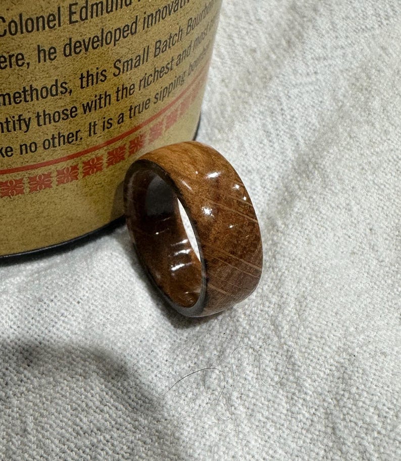 Puede incluir: Un anillo de madera de color marr&oacute;n intenso, con la veta de la madera visible. El anillo es liso y pulido, con un acabado ligeramente brillante. Una joya &uacute;nica.