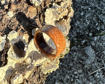 May include: A wooden ring with a textured, grid-like pattern on the exterior. The ring has a warm, brown color with darker brown accents. The ring is made of wood and has a smooth, polished finish.
