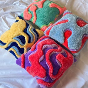 Può includere: Quattro cuscini decorativi quadrati con disegni astratti. I cuscini presentano colori vivaci tra cui giallo, blu, verde, rosso e viola. Ogni cuscino ha un motivo unico, creando un'estetica giocosa e artistica.