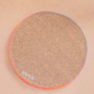 May include: A round rug with a light brown center and a colorful border. The border transitions from orange to pink to blue. The rug has the text "RUGU" in the lower left corner.
