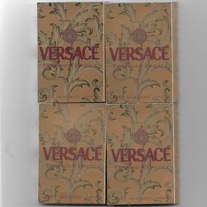 May include: Four miniature perfume bottles with gold and brown packaging. Each bottle features the text "VERSACE Emotional Essence" and "EAU DE TOILETTE 0.05 FL OZ".