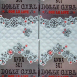May include: Four miniature perfume bottles with a white background and black and red floral designs. The bottles are labelled "Anna Sui Dolly Girl Ooh La Love".