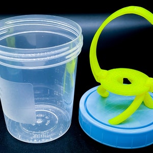 May include: A clear plastic container with a blue lid and a yellow plastic handle. The container has markings for measuring liquids in ounces and milliliters. The handle is attached to the lid and has a circular base.