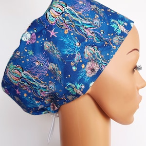 May include: Blue surgical scrub hat with a colorful jellyfish and starfish pattern. The hat has a white drawstring.