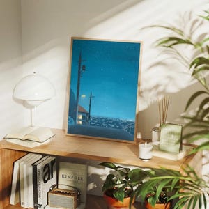 May include: A framed art print depicts a nighttime cityscape under a starry sky. The artwork features a road, streetlights, and a house with lit windows. The print is displayed on a wooden shelf with books, a lamp, and a candle.