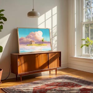 May include: A framed art print showing a house on an island with a tree, set against a blue sky and pink clouds. The artwork is displayed on a mid-century wooden cabinet. The cabinet is 150 cm long.