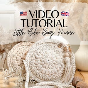 以下が含まれることがあります： クリーム色の丸い編み物のバッグが2つ、長いクリーム色のストラップが付いています。右側のバッグには木製のビーズとクリーム色のタッセルが付いています。バッグの上に「VIDEO TUTORIAL Little Boho Bag 'Marie'」というテキストが表示されています。