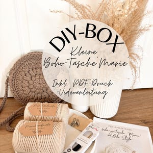 Könnte beinhalten: DIY-Set für eine kleine Boho-Tasche namens "Marie". Das Set enthält zwei Spulen mit naturfarbenem Kordel, eine Häkelnadel, einen Metallring und eine gedruckte Anleitung. Die Tasche ist aus naturfarbenem Kordel gefertigt und hat eine runde Form.