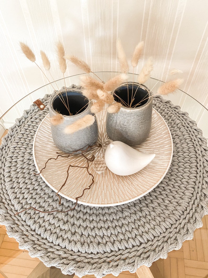 Puede incluir: Dos jarrones de cer&aacute;mica gris con hierba de la pampa seca sobre un camino de mesa redondo de crochet gris. Una figurita de p&aacute;jaro de cer&aacute;mica blanca est&aacute; sobre un plato de cer&aacute;mica beige.
