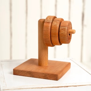 Könnte beinhalten: Holzspielzeug mit Stapelringen in natürlicher Holzoptik. Die Ringe sind auf einem Holzständer mit quadratischer Basis gestapelt.