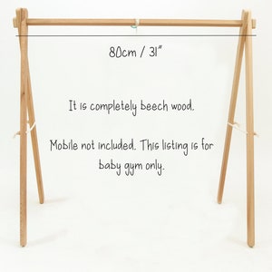 May include: A wooden baby gym stand made of beech wood. The stand is 31 inches wide and 31 inches tall. The text "80cm / 31" is written on the stand. The text "It is completely beech wood. Mobile not included. This listing is for baby gym only." is written below the stand.