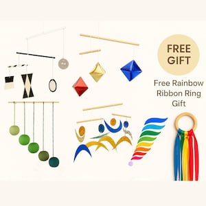 May include: A selection of contemporary mobiles in diverse designs and colours. The mobiles showcase geometric shapes, spheres, and abstract forms suspended from wooden dowels. A rainbow ribbon ring is also included as a free gift.