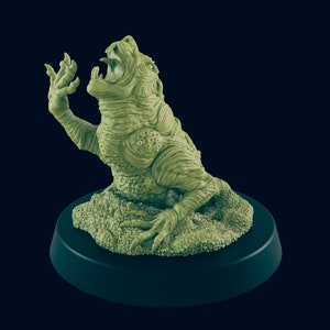 May include: A green, detailed, miniature figurine of a creature with a large mouth and claws, standing on a green base. The creature is posed in a defensive stance, with its claws raised and its mouth open in a roar.