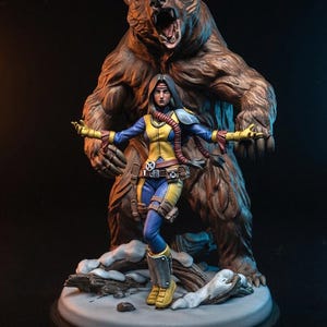 May include: A detailed figurine of a woman in a blue and yellow costume, arms outstretched, with a large brown bear behind her. The base is a snowy landscape. The text "MIRAGE" and "40MM SCALE | 3D PRINTING STL (PRESUPPORTED)" are at the bottom.