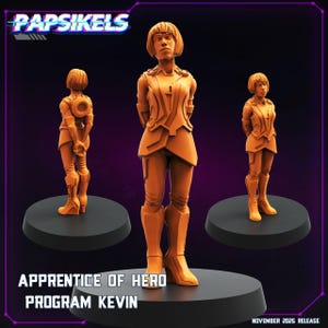 May include: Three orange figurines of a person in a futuristic outfit, standing on black circular bases. The text "Papsikels" is at the top, and "Apprentice of Hero Program Kevin" is at the bottom. The release date is November 2025.