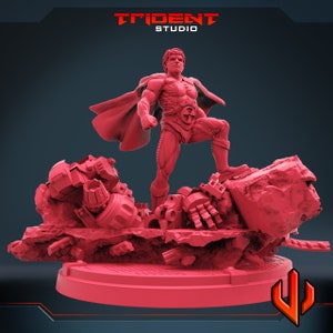 Puede incluir: Una figura en miniatura de plástico rojo de un superhéroe de pie sobre una base de piezas robóticas rotas. El superhéroe lleva una capa roja y un traje rojo y negro. La base está hecha de plástico gris y tiene una superficie texturizada.