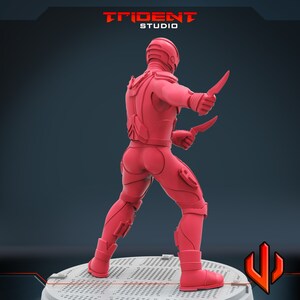 Pu&ograve; includere: Una action figure rossa di un guerriero futuristico con un elmetto e due coltelli. La figura &egrave; in piedi su una base circolare con un motivo a griglia.