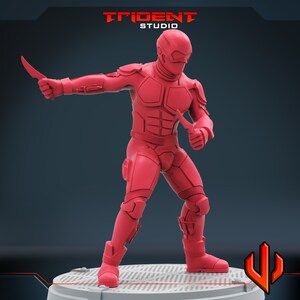 Pu&ograve; includere: Una action figure rossa di un soldato futuristico con un elmetto e due coltelli. La figura &egrave; in piedi su una base grigia con uno sfondo nero.