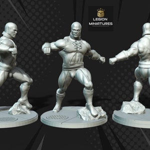 May include: A gray plastic miniature figurine of a superhero in a fighting pose. The figure is standing on a round base with a textured surface. The figure is wearing a costume with a symbol on the chest. The figure is posed with one arm raised and the other arm extended forward.