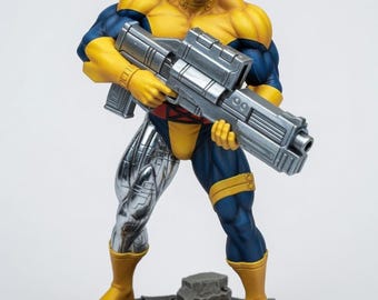 May include: A detailed figurine of a muscular character with long black hair and a mustache, wearing a yellow and blue suit. The figure has a metallic silver right leg, holds a large silver futuristic rifle, and stands on a circular base.