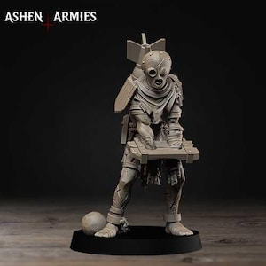 以下が含まれることがあります： ASHEN ARMIESと記された灰色のミニチュアフィギュア。マスクを被り、ボロボロの服を着た人型のキャラクターが、背中に大きな爆弾を背負い、木箱を抱えています。足首には足枷がはめられており、円形の台座の上に立っています。
