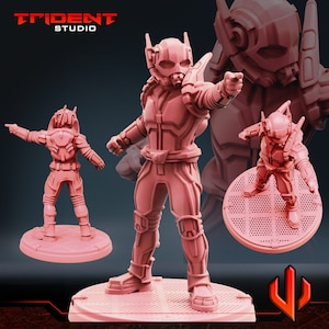 Op de afbeelding: Roze Ant-Man-figuur, met een gedetailleerde helm en pak, in een dynamische pose. Het figuur staat op een cirkelvormige basis met een rasterpatroon. Het Trident Studio-logo is zichtbaar.