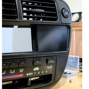 May include: Black car dashboard with a digital display screen, climate control buttons, and a defroster button. The buttons are labelled "OFF", "1", "2", "3", "4", and "A/C".