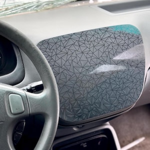 Könnte beinhalten: Nahaufnahme des Innenraums eines Autos mit einer Armaturenbrett-Abdeckung mit geometrischem Muster. Die Abdeckung besteht aus einem klaren Material mit einem schwarzen geometrischen Muster.