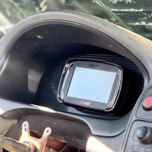 Può includere: Un cruscotto nero con uno schermo digitale. Lo schermo mostra "FT 450" in testo rosso. Il cruscotto fa parte dell'interno di un veicolo, con un parabrezza rotto sullo sfondo.