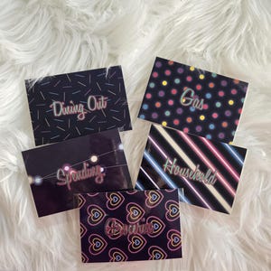 May include: A collection of six black and neon-colored budget cards. Each card features a different category: "Dining Out," "Gas," "Spending," "Household," and "Groceries." The cards have various designs, including dots, stripes, and heart patterns.