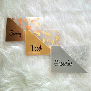May include: Three clear acrylic budget organizers with metallic accents. Each organizer has a diagonal section in gold, copper, or silver, with gold, copper, or silver foil flakes. The labels read "Beauty", "Food", and "Groceries".