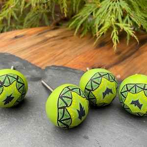 May include: Four green and black patterned ceramic knobs with a starburst design. The knobs are round and have a shiny finish.