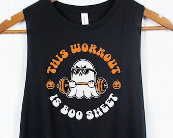 May include: Black sleeveless tank top with a white graphic of a ghost wearing sunglasses and lifting a barbell with pumpkins on each side. The text "This Workout Is Boo Sheet" is written in a white circle around the ghost.