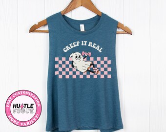 May include: A teal blue sleeveless tank top with a pink and white checkered pattern and a ghost holding a pink dumbbell. The text "Creep It Real" is printed in white above the ghost.
