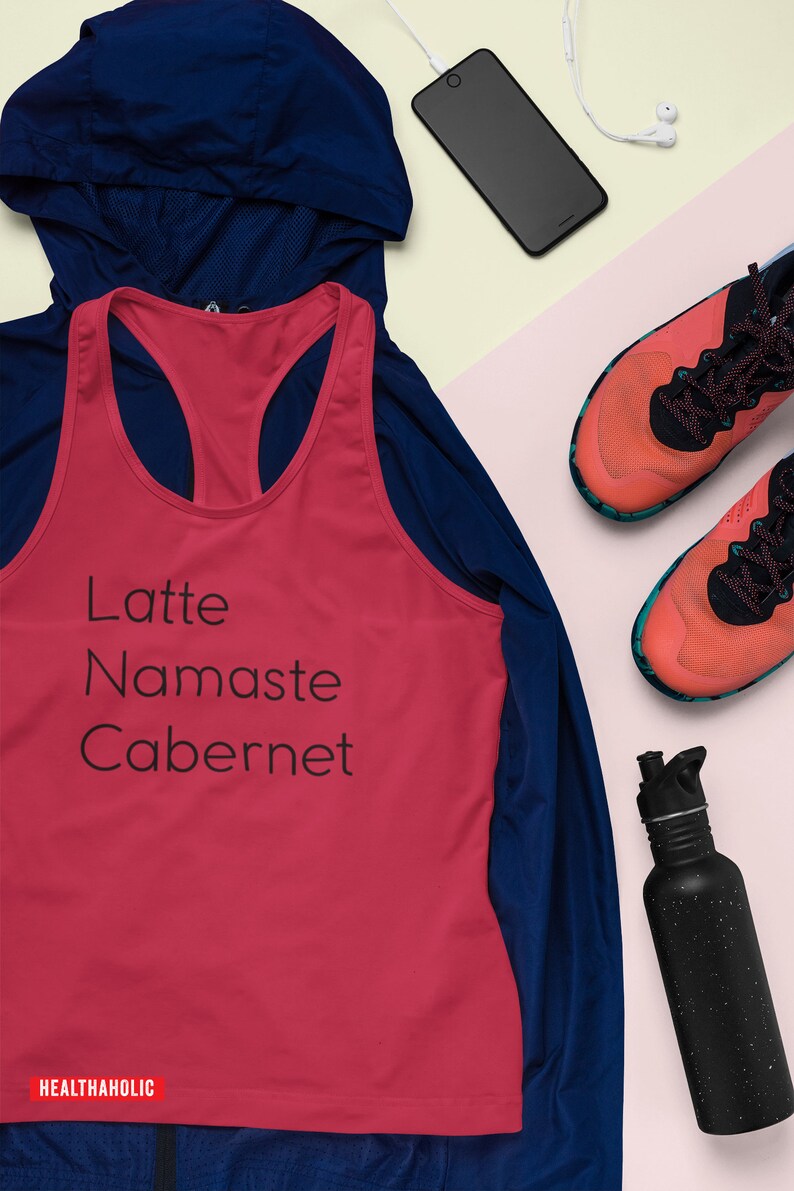 Pu&ograve; includere: Un top rosso senza maniche con il testo "Latte Namaste Cabernet" e la parola "HEALTHAHOLIC" in basso. Il top &egrave; sovrapposto a una giacca blu. L'immagine include anche una bottiglia d'acqua nera, un paio di scarpe da corsa arancioni e nere, uno smartphone nero e auricolari bianchi.