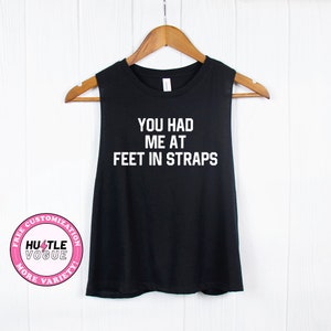 May include: Black sleeveless tank top with the text "You had me at feet in straps" in white.