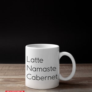 Pu&ograve; includere: Tazza in ceramica bianca con testo nero che recita "Latte, Namaste, Cabernet".