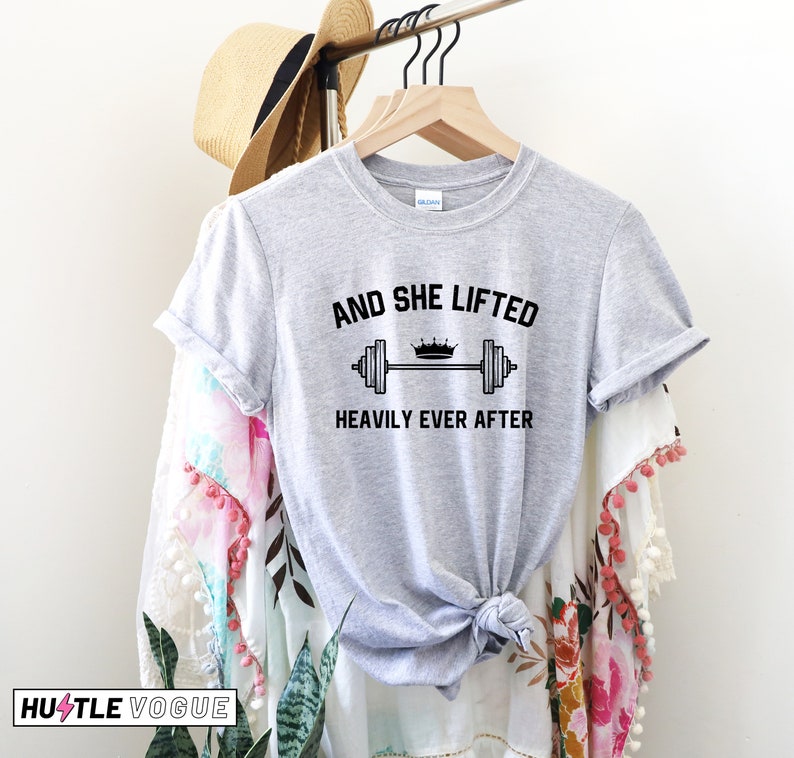 May include: Gray t-shirt with the text "And she lifted heavily ever after" and a graphic of a barbell with a crown on top.