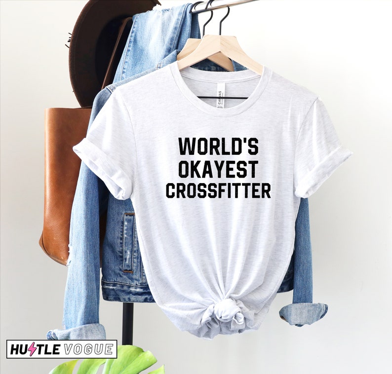 May include: White t-shirt with black text that reads "WORLD'S OKAYEST CROSSFITTER".