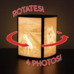 May include: A rotating lamp with four photo panels. The lamp displays images of dogs in sepia tones. The text "ROTATES!" and "4 PHOTOS!" are in red. The lamp is on a dark surface.