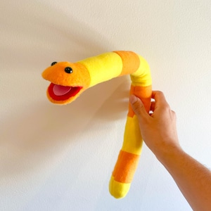May include: A yellow and orange striped plush worm puppet with a wide open mouth and black eyes.