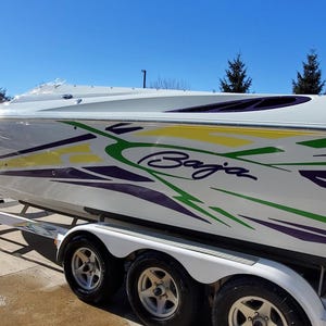 May include: A white Baja boat with green, yellow and purple racing stripes. The boat is on a trailer with three wheels.