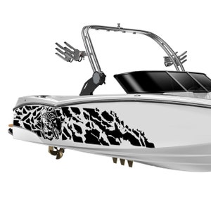 May include: A white boat with a black and white camouflage design on the side. The boat has a tower with a wakeboard rack and a black windscreen.