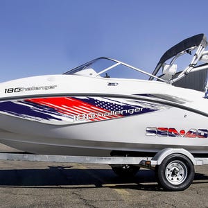 Puede incluir: Barco Sea-Doo 180 Challenger blanco sobre un remolque. El barco tiene un dise&ntilde;o gr&aacute;fico rojo, blanco y azul en el lateral. El barco est&aacute; en un remolque con una rueda de repuesto. El barco tiene un parabrisas y una capota negra.