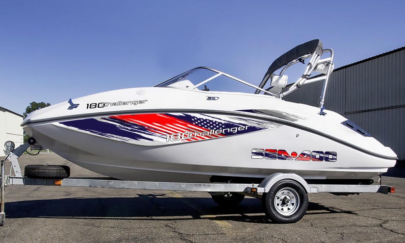 Puede incluir: Barco Sea-Doo 180 Challenger blanco sobre un remolque. El barco tiene un dise&ntilde;o gr&aacute;fico rojo, blanco y azul en el lateral. El barco est&aacute; en un remolque con una rueda de repuesto. El barco tiene un parabrisas y una capota negra.