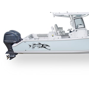 May include: A white boat with a black fish decal on the side. The decal has the text "YOUR NAME" below the fish. The boat has a white hardtop and a black outboard motor.