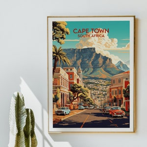 May include: A vintage travel poster featuring a colorful illustration of Cape Town, South Africa. The poster depicts a street scene with buildings, palm trees, and cars. The iconic Table Mountain is visible in the background.
