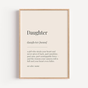 Op de afbeelding: Een printbare definitie van het woord "Dochter" in een minimalistische zwart-wit stijl. De definitie luidt: "Een meisje dat je hart steelt en het nooit teruggeeft. Deel zonneschijn, deel pit, deel onstuitbare kracht - en de reden waarom je camera rol vol is en je hart nog voller. Zie ook: naam"