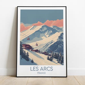 Op de afbeelding: Een ingelijste kunstprint met een vintage-stijl illustratie van Les Arcs, Frankrijk. Het kunstwerk toont besneeuwde bergen, skiliften en gebouwen, met een blauwe en roze lucht. De tekst "LES ARCS FRANCE" staat onderaan.